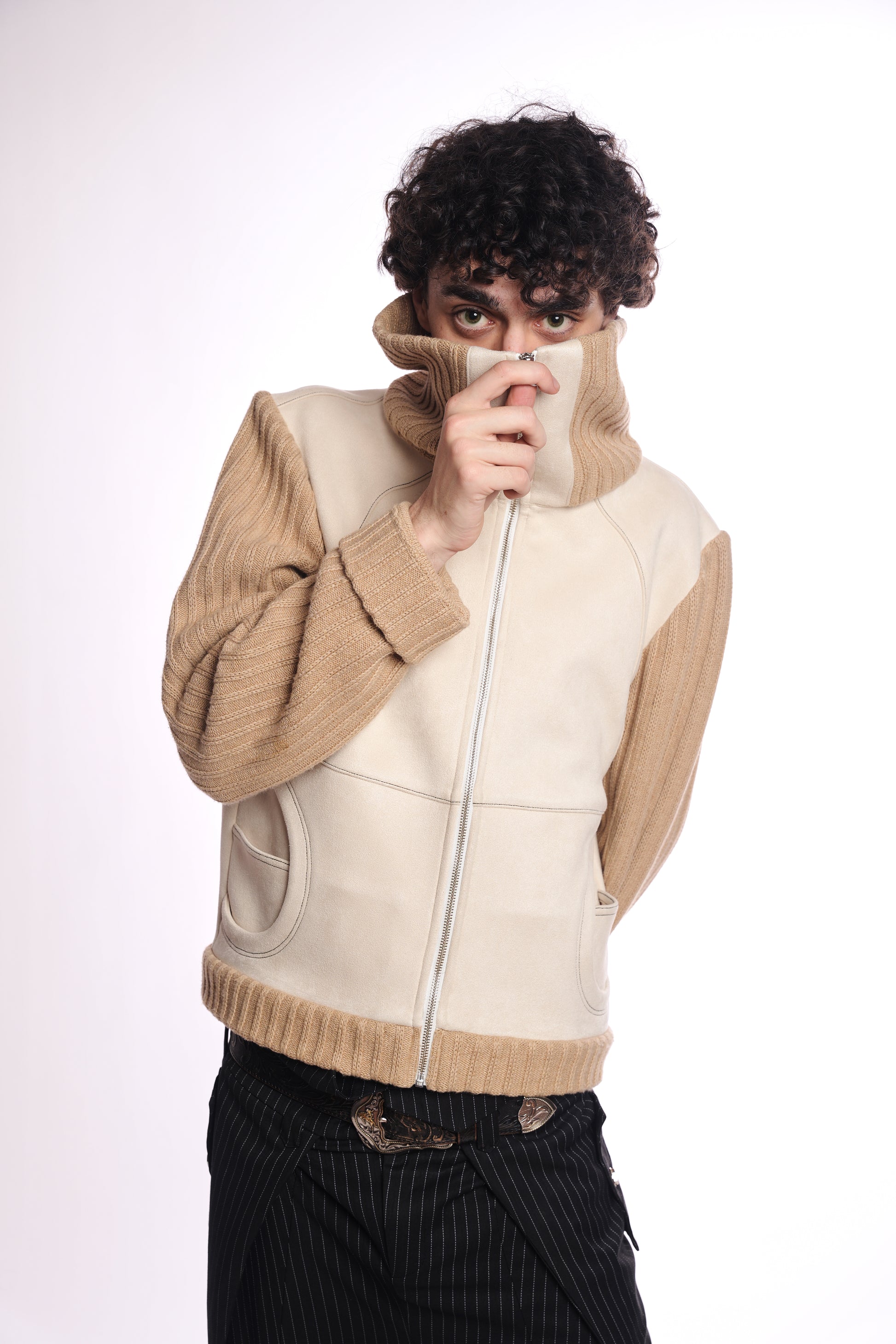 Person wearing a beige and cream jacket with a unique design on a white background