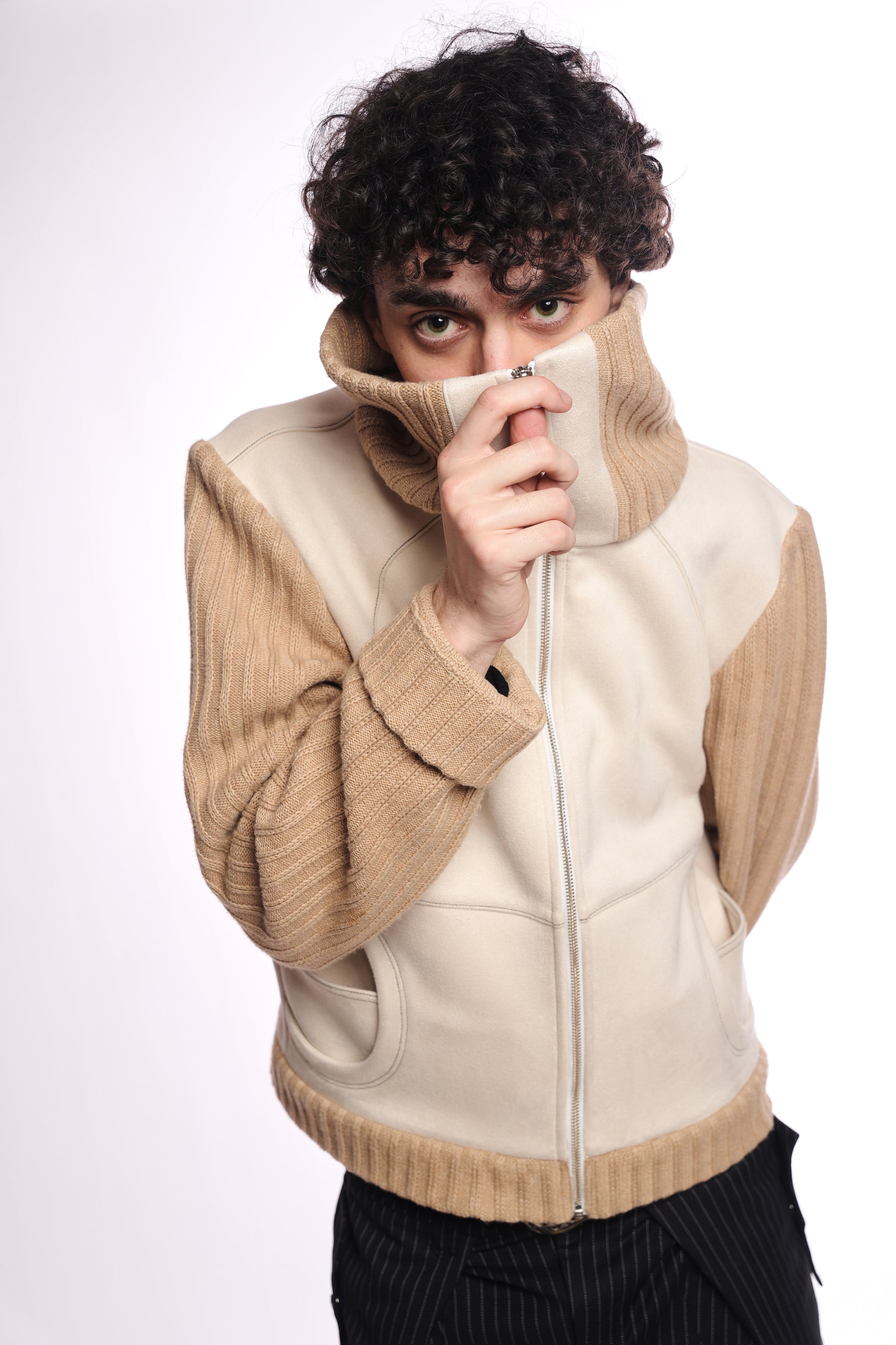 Person wearing a beige and white jacket with a plain background collar zipped up