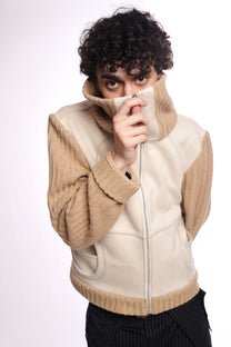 Person wearing a beige and white jacket with a plain background collar zipped up