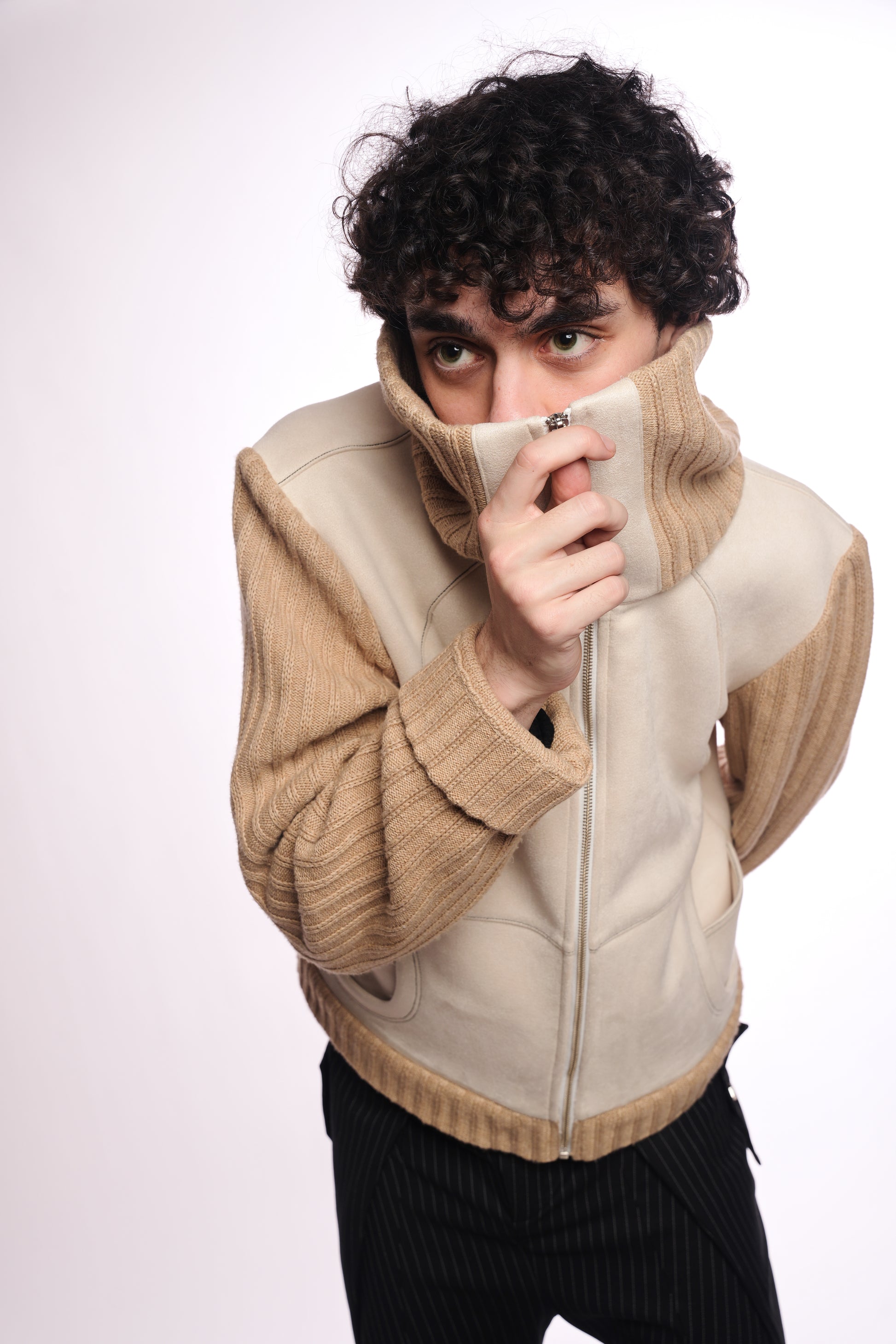 Person wearing a beige sweater over a white shirt with a plain background