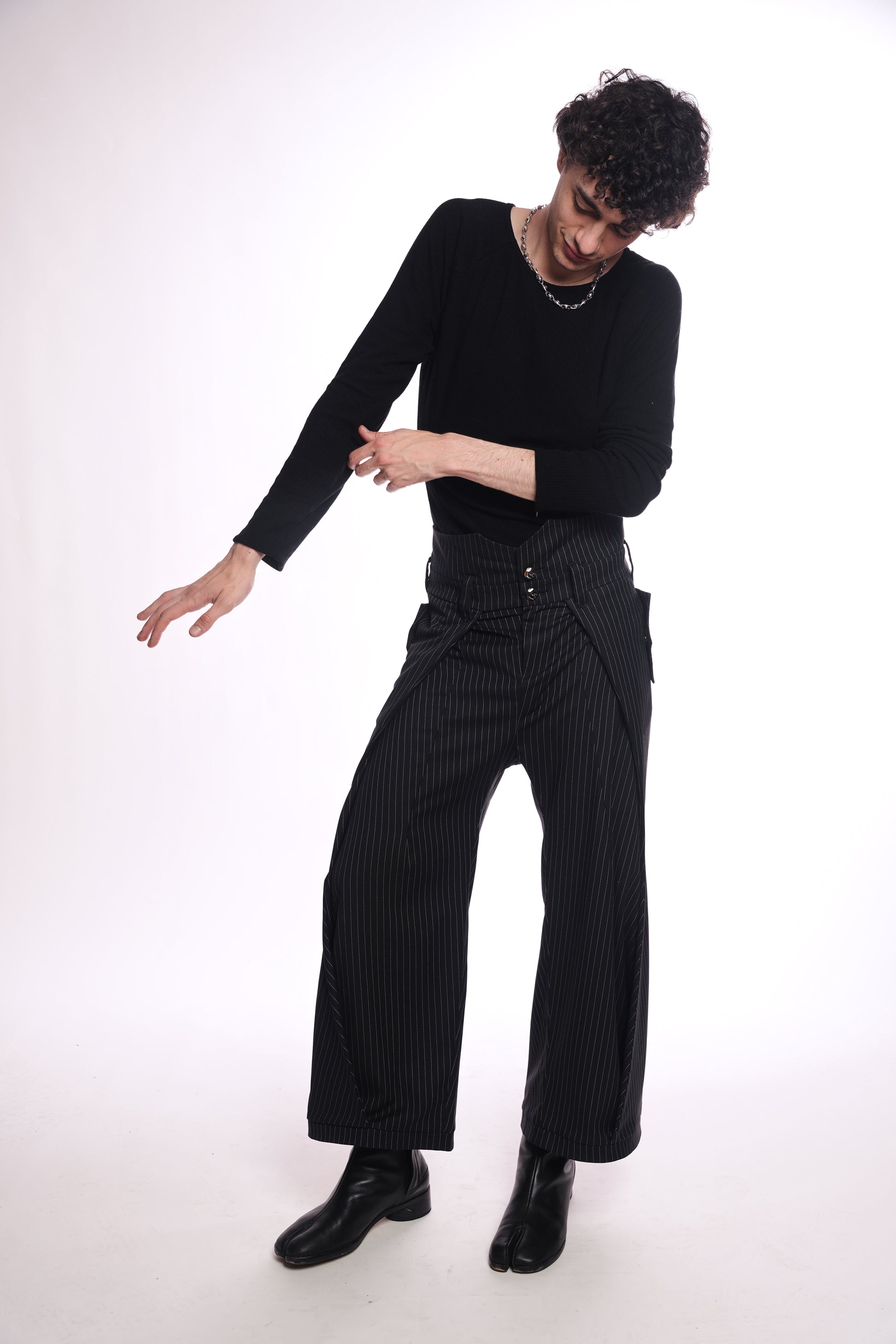 Person wearing a black outfit with a black top and black pinstripe pants on a white background