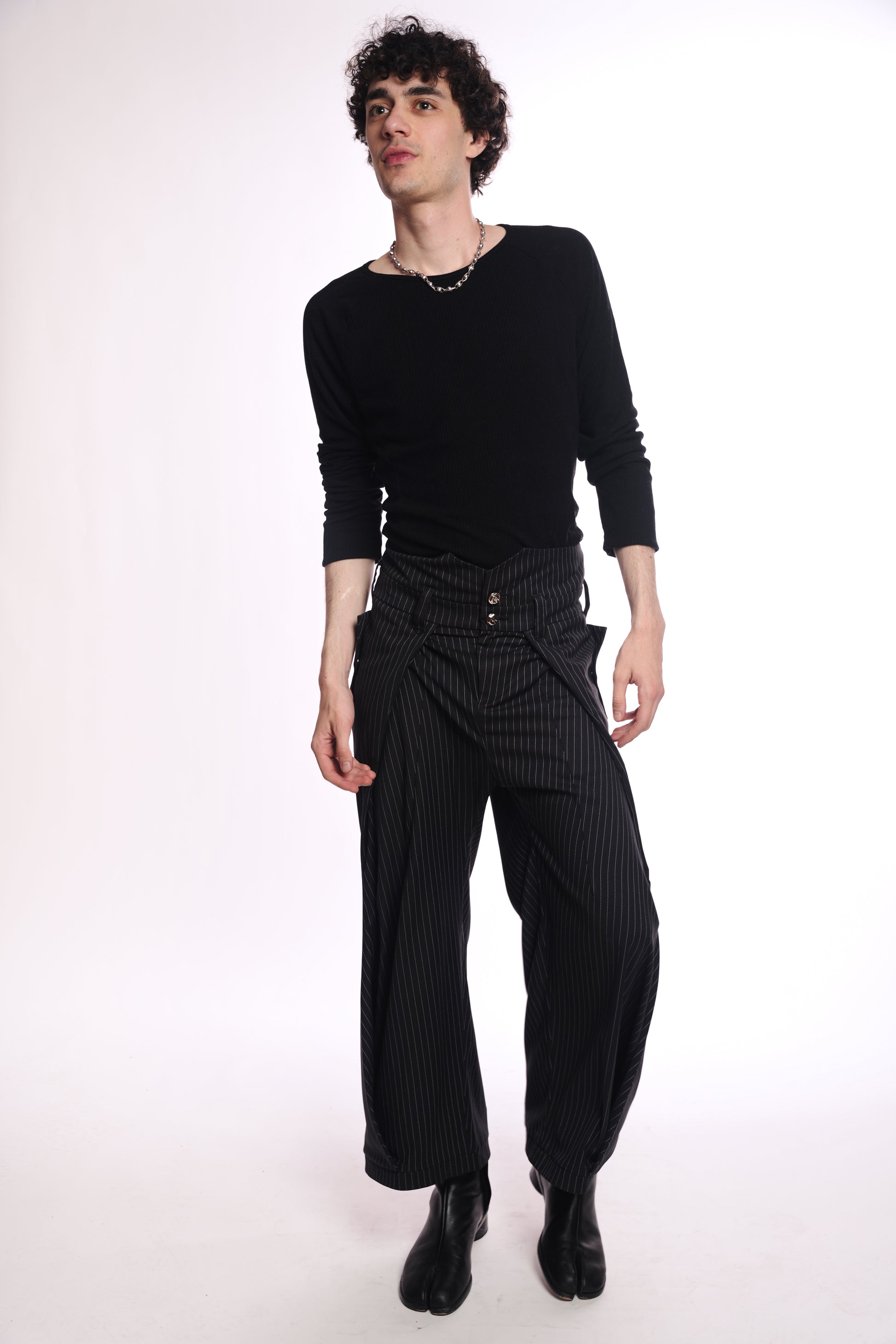 Person wearing a black outfit with (origami pants) on a white background